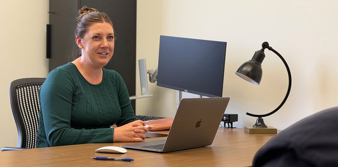 Woman seated at a desk using a laptop during a meeting in a professional office setting