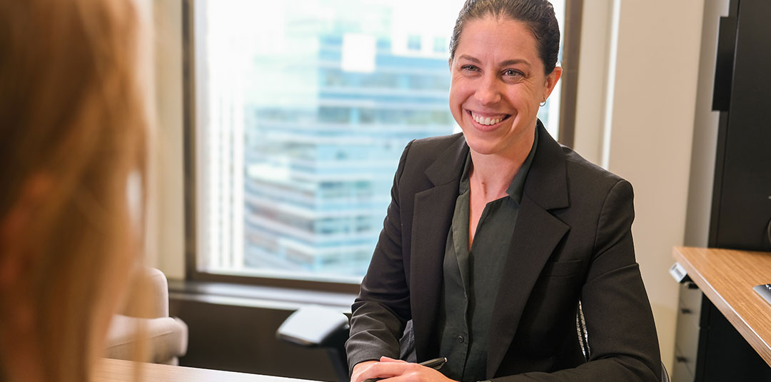 Professional woman smiling while seated at a desk during a meeting in a modern office setting.