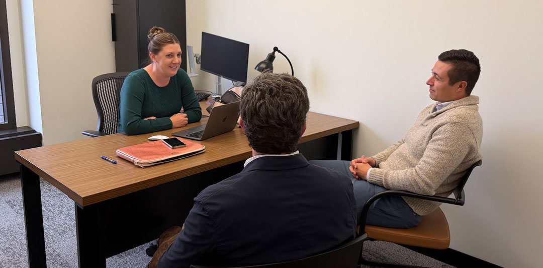 Two people meeting at a desk with a laptop in an professional office setting.